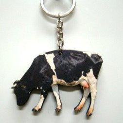 Houten sleutelhanger in de vorm van een zwart-witte koe die met de kop naar beneden staat te grazen, bevestigd aan een metalen ketting en sleutelring.